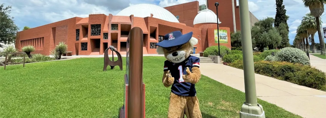 Wilbur the Wildcat giving "finger guns" in front of the Flandrau Science Center and Planetarium